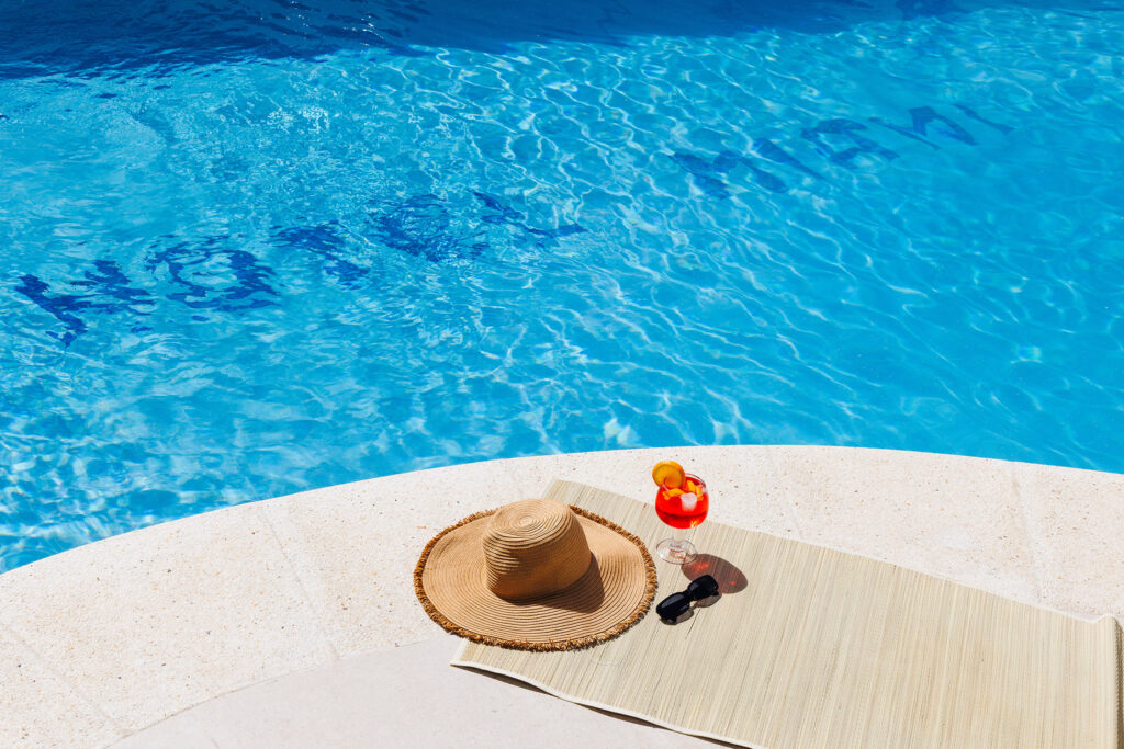 Piscina cristalina con aperol y gafas de sol en el borde