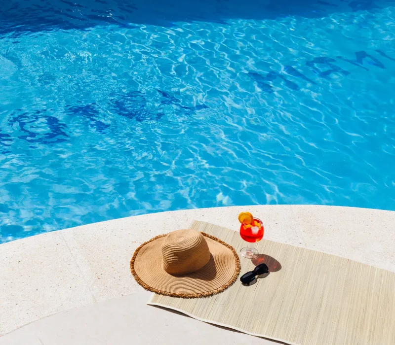 Foto bordillo de la piscina aguas cristalinas azules con aperol+gafas de sol+sombrero de paja